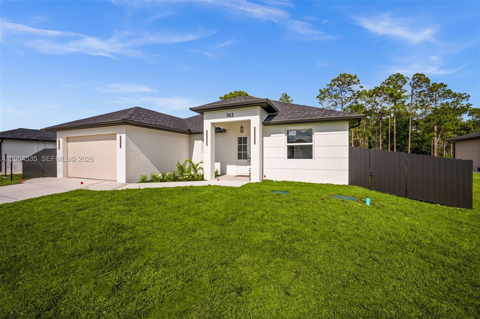 A single-story house with a white stucco exterior, dark roof, and a front-facing garage — 763 Andover Ave S, Lehigh Acres FL 33974, LEHIGH ACRES, FL