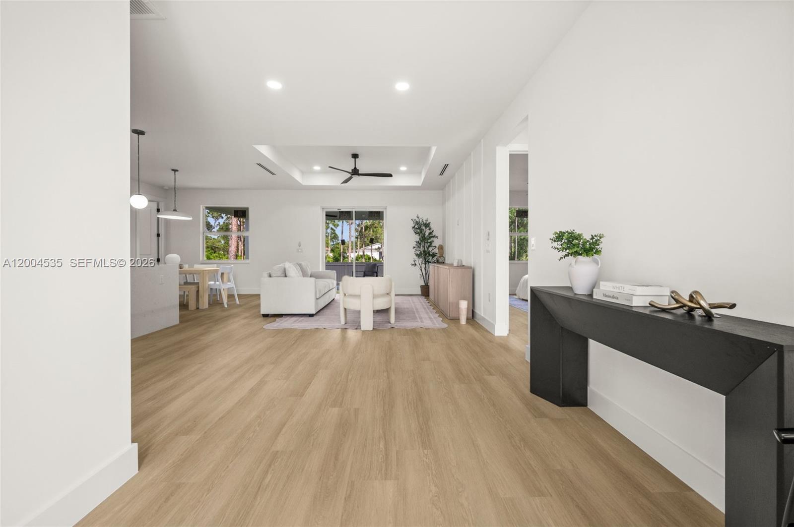 A bright, open-concept living and dining area features light wood flooring and a tray ceiling — 763 Andover Ave S, Lehigh Acres FL 33974, LEHIGH ACRES, FL