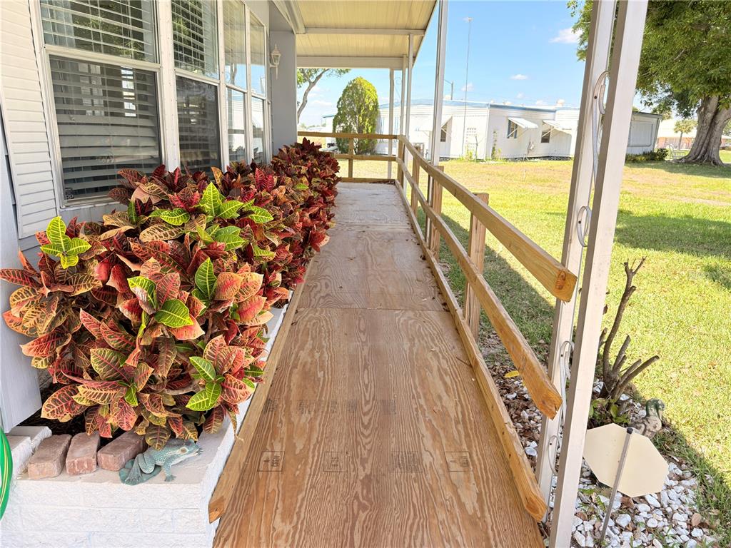 A wooden wheelchair ramp runs alongside a house exterior with a row of croton plants — 2202 BAHAMA ROAD W, SEBRING, FL