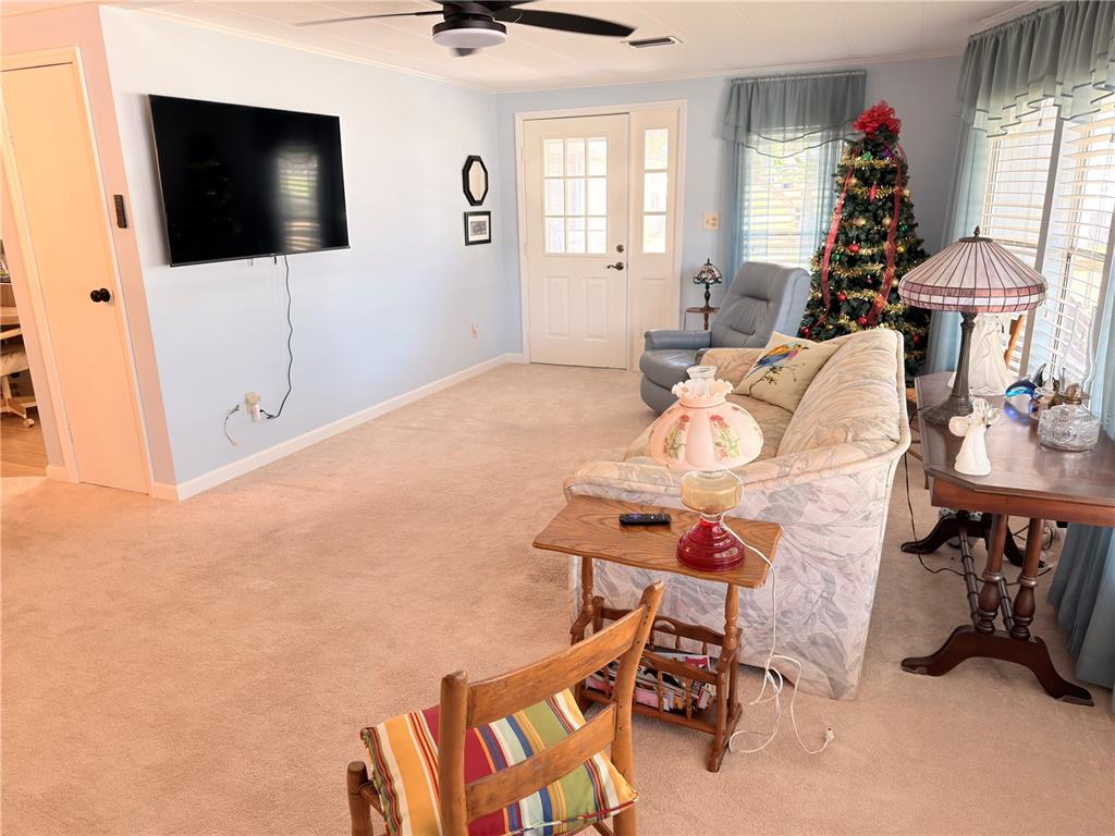 A living room features light blue walls, beige carpeting, a television, and a Christmas tree — 2202 BAHAMA ROAD W, SEBRING, FL