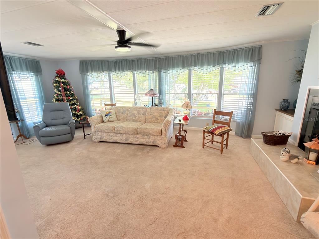 A living room features a beige sofa, blue recliner, carpeted flooring, and large windows — 2202 BAHAMA ROAD W, SEBRING, FL