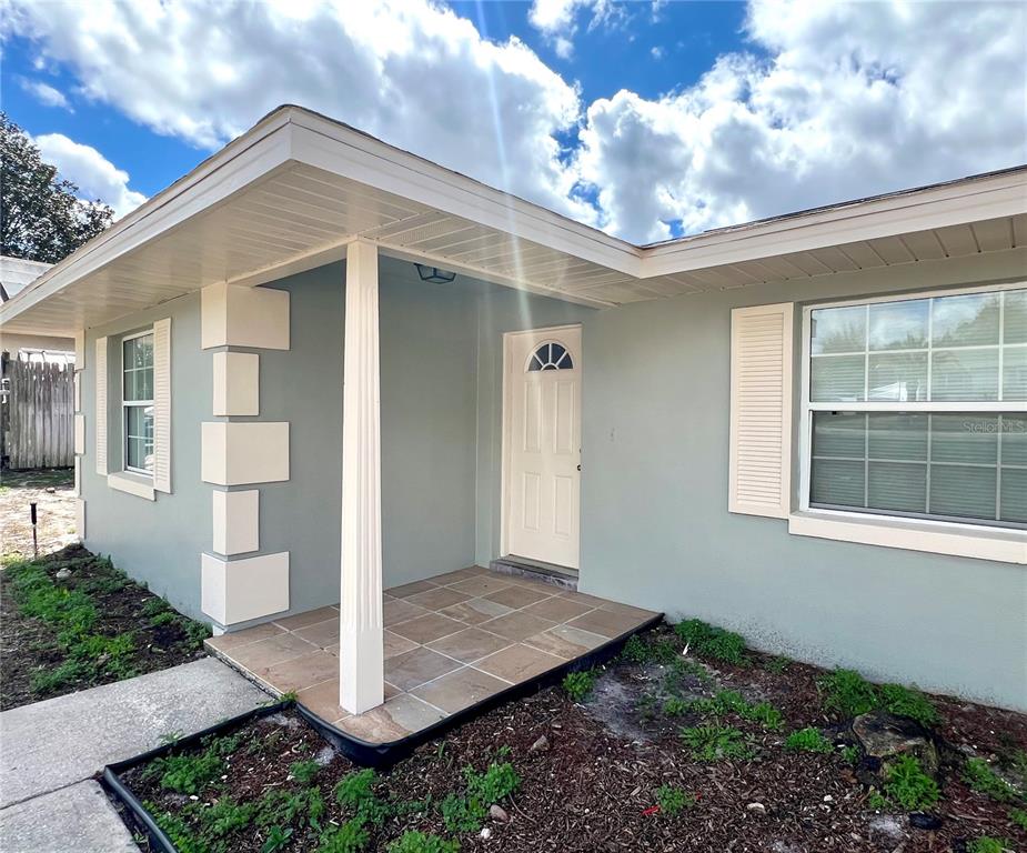 A light green house exterior features a covered porch with tiled flooring and white shutters — 2338 FITZPATRICK TERRACE, DELTONA, FL