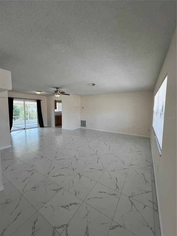 A spacious living room features white marble-look tile flooring, a ceiling fan, and sliding doors — 2338 FITZPATRICK TERRACE, DELTONA, FL