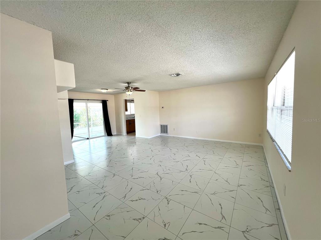 A spacious living area features white marble-look tile flooring, a ceiling fan, and sliding glass doors — 2338 FITZPATRICK TERRACE, DELTONA, FL