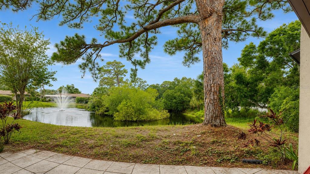 A paved patio overlooks a pond with a fountain, surrounded by trees and landscaping — 947 SUNRIDGE WAY UNIT A3, SARASOTA, FL