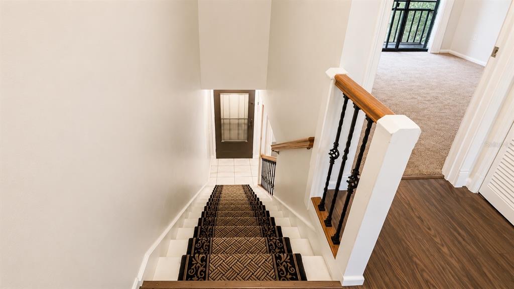 A staircase with a patterned runner leads down to a tiled entryway and front door — 947 SUNRIDGE WAY UNIT A3, SARASOTA, FL
