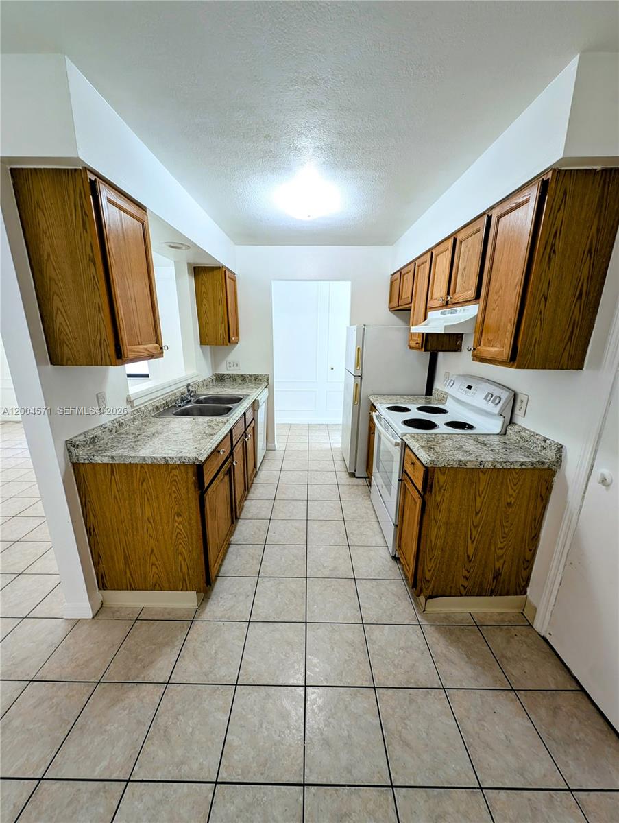 A galley kitchen features wood cabinets, granite-look countertops, white appliances, and light tile flooring — 915 Turtle Cove Ln, Vero Beach FL 32963, VERO BEACH, FL