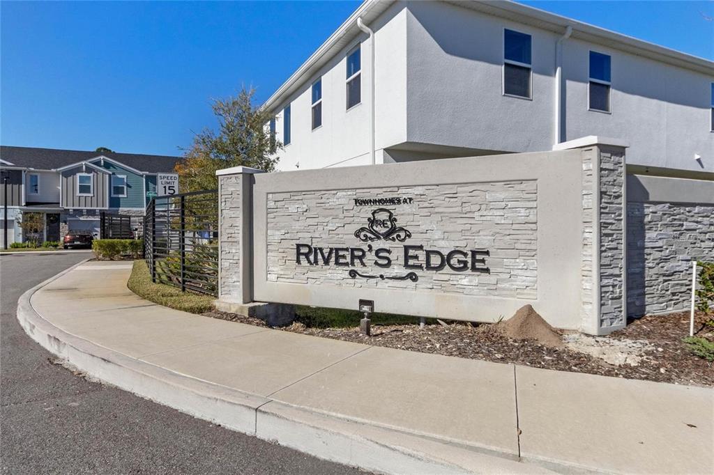 A stone monument sign for Townhomes at River's Edge sits beside a sidewalk and building — 1345 CAPTIVA COVE, SANFORD, FL