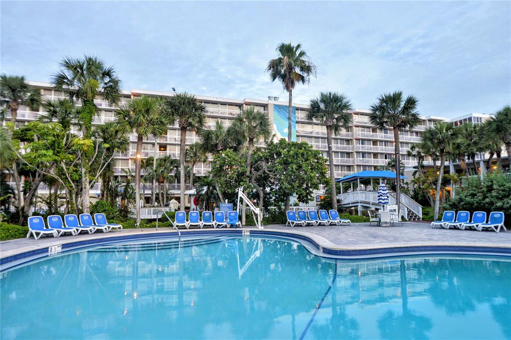 A swimming pool sits in front of a multi-story resort building surrounded by palm trees — 5500 GULF BOULEVARD UNIT 6241, ST PETE BEACH, FL
