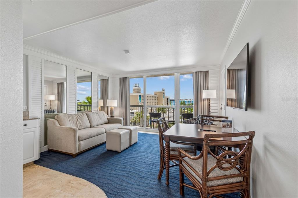 A living and dining area features a blue carpet, beige sofa, and a balcony view — 5500 GULF BOULEVARD UNIT 6241, ST PETE BEACH, FL