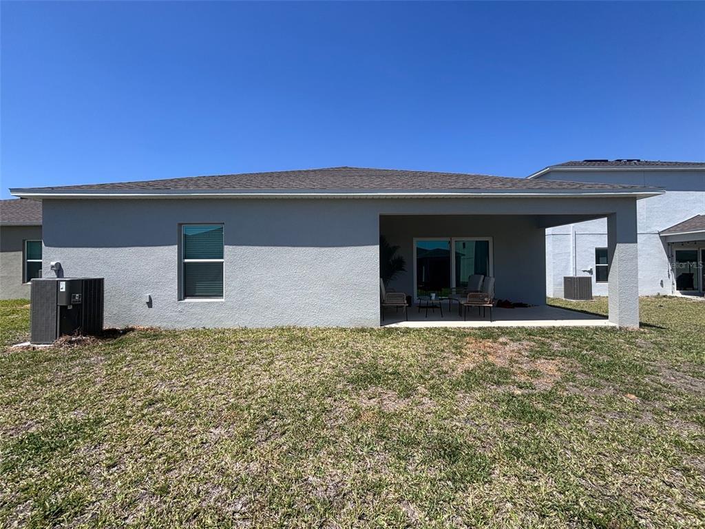 The rear exterior of a gray stucco house features a covered patio and a lawn — 4762 VELLACITO WAY, DAVENPORT, FL