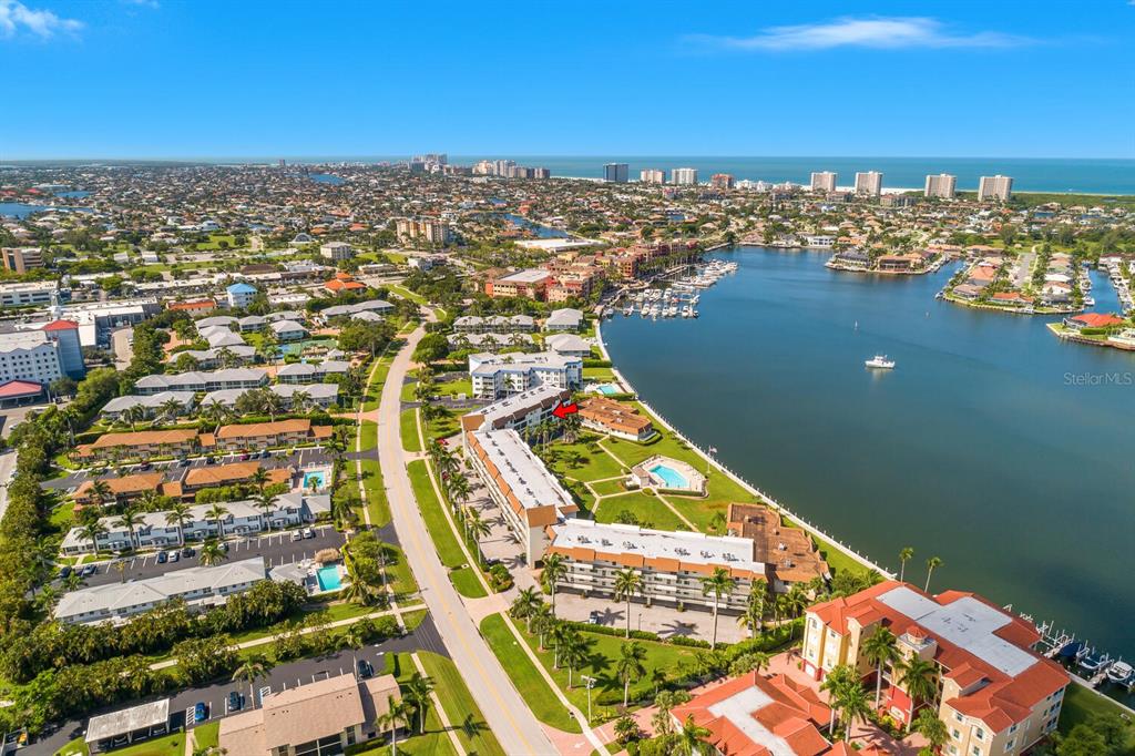 An aerial view shows a multi-story waterfront apartment complex with a pool and boat docks — 730 W ELKCAM CIRCLE UNIT 302, MARCO ISLAND, FL