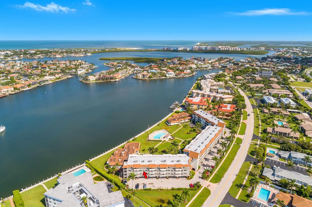 An aerial view shows a multi-story apartment building with a red arrow pointing to it — 730 W ELKCAM CIRCLE UNIT 302, MARCO ISLAND, FL