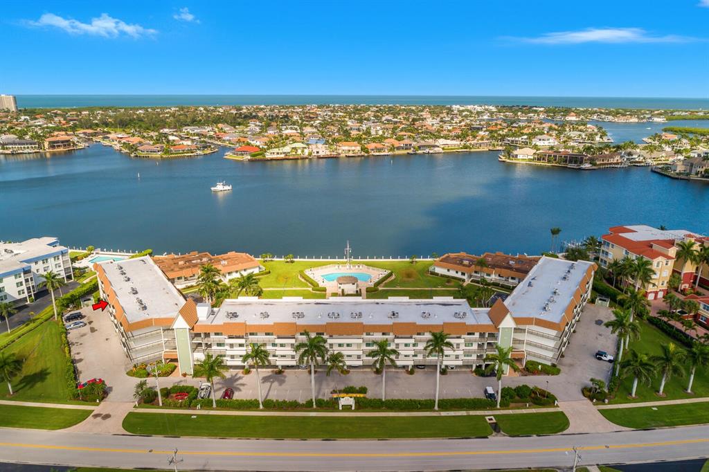 An aerial view shows a multi-story apartment complex with a pool overlooking a bay — 730 W ELKCAM CIRCLE UNIT 302, MARCO ISLAND, FL