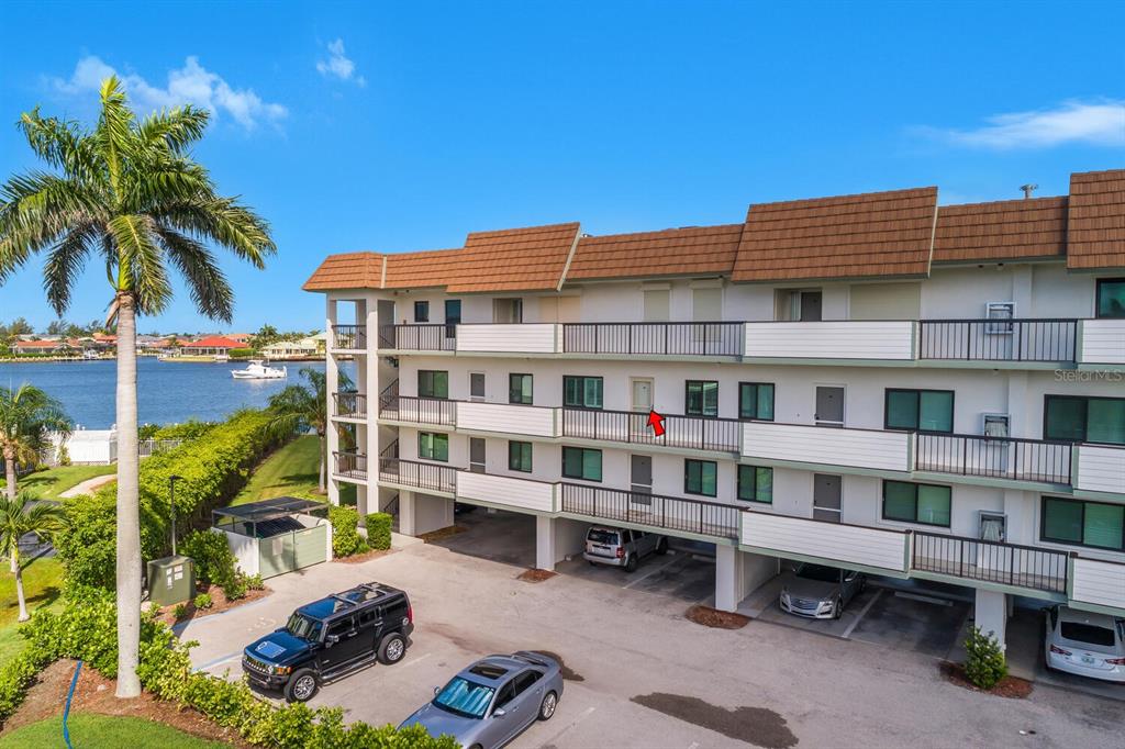 An exterior view of a multi-story apartment building with covered parking and a waterfront location — 730 W ELKCAM CIRCLE UNIT 302, MARCO ISLAND, FL