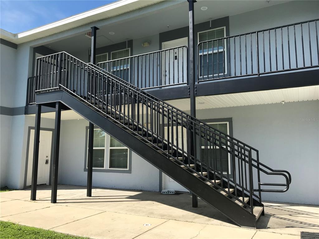 An exterior view of a two-story apartment building with a black metal staircase and railings — 284 GARDNER LANE UNIT A, KISSIMMEE, FL