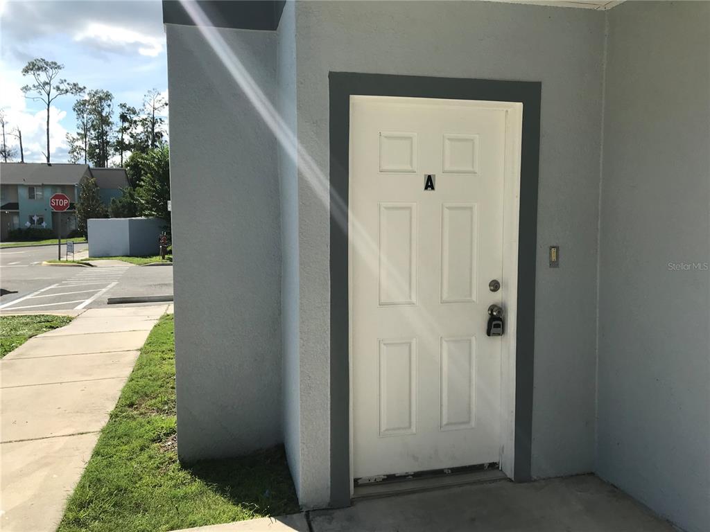 A white exterior door labeled A is set into a gray wall near a sidewalk — 284 GARDNER LANE UNIT A, KISSIMMEE, FL