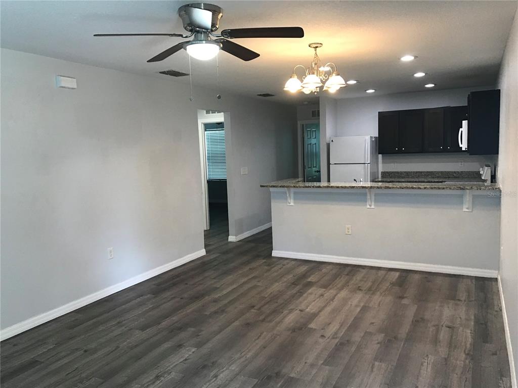 An open-concept living area features gray wood-look flooring, a ceiling fan, and a kitchen breakfast bar — 284 GARDNER LANE UNIT A, KISSIMMEE, FL