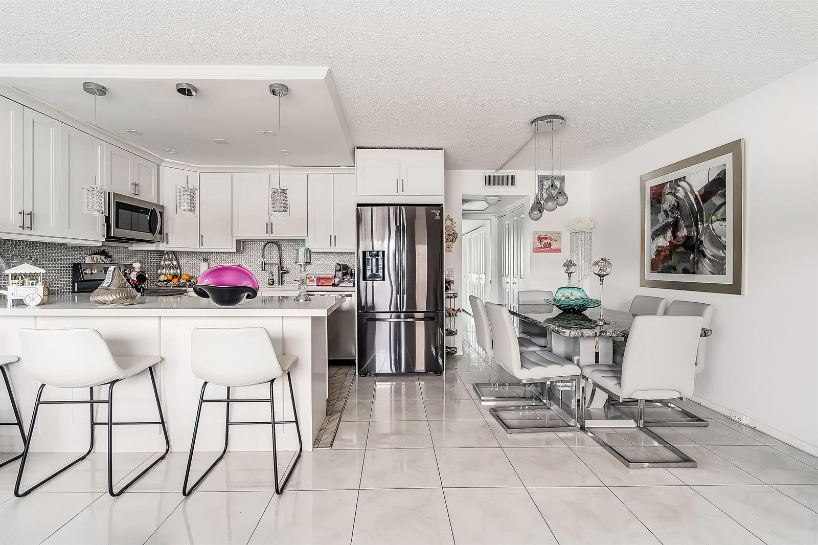 A modern kitchen and dining area with white cabinetry, stainless steel appliances, and tile flooring — 1012 Lincoln # 1012, Boca Raton FL 33434, BOCA RATON, FL