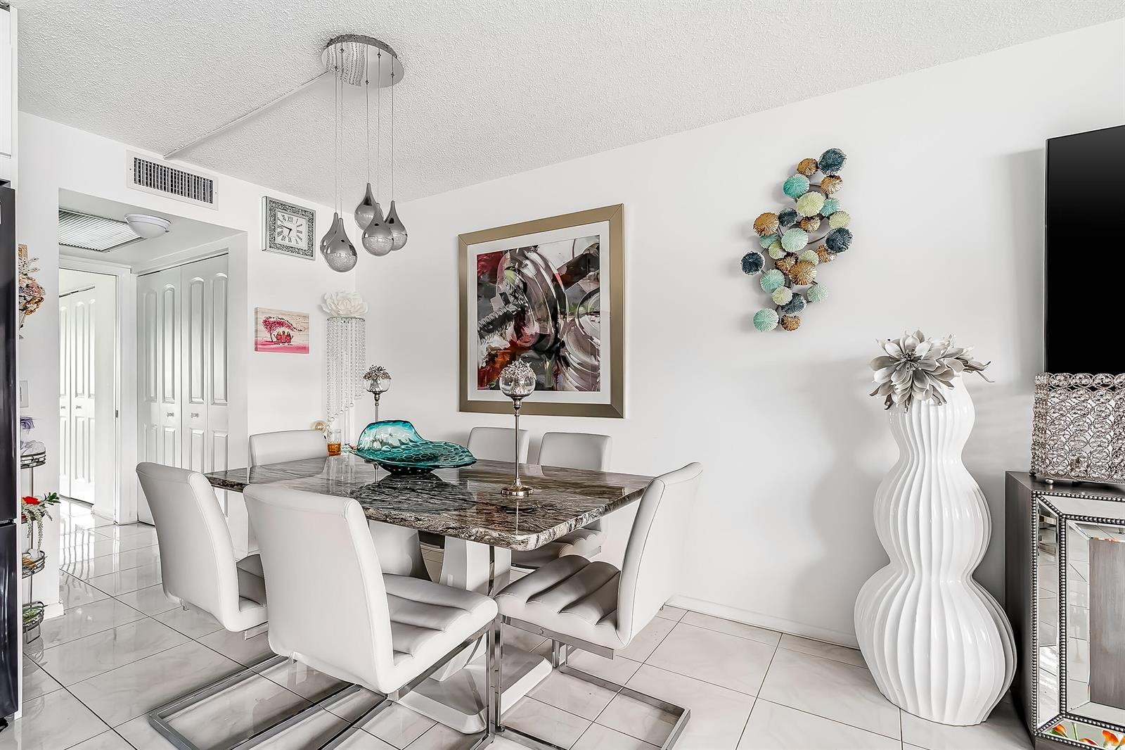 A dining room features a marble-topped table, white chairs, modern pendant lighting, and wall art — 1012 Lincoln # 1012, Boca Raton FL 33434, BOCA RATON, FL