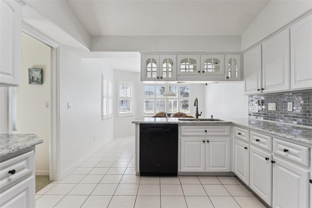 A kitchen with white cabinets, granite countertops, a black dishwasher, and white tile flooring — 5811 PRINCESS CAROLINE PLACE, LEESBURG, FL