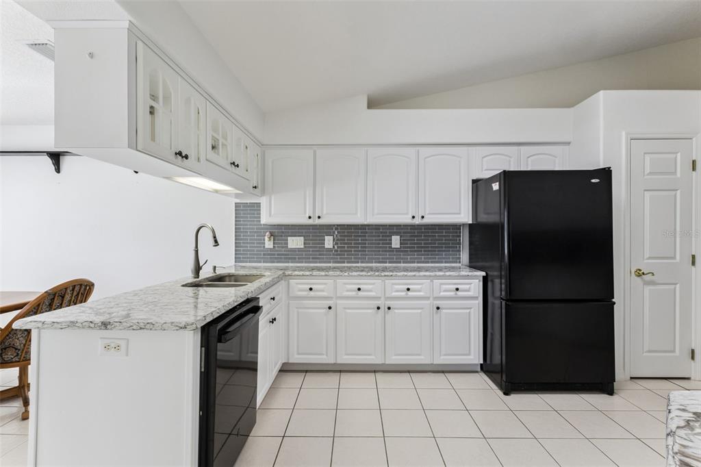 A kitchen features white cabinets, granite countertops, a gray subway tile backsplash, and black appliances — 5811 PRINCESS CAROLINE PLACE, LEESBURG, FL
