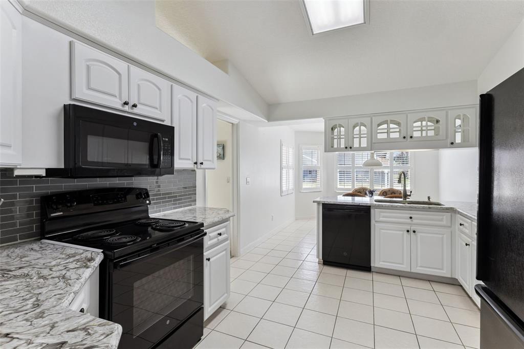 A kitchen with white cabinets, black appliances, gray tile backsplash, and white tile flooring — 5811 PRINCESS CAROLINE PLACE, LEESBURG, FL