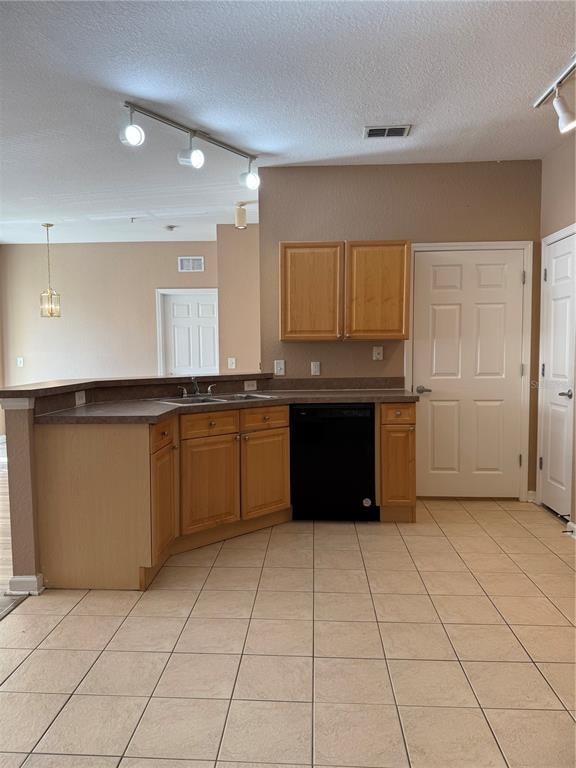 A kitchen features light wood cabinets, dark countertops, a black dishwasher, and beige tile flooring — 413 TERRACE RIDGE CIRCLE UNIT 413, DAVENPORT, FL