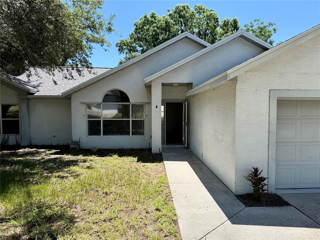 The exterior of a single-story house features a white stucco facade and a concrete walkway — 10258 JOANIES RUN, LEESBURG, FL