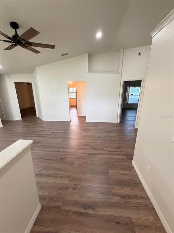 An open-concept living area features vaulted ceilings, wood-look flooring, and three doorways — 10258 JOANIES RUN, LEESBURG, FL