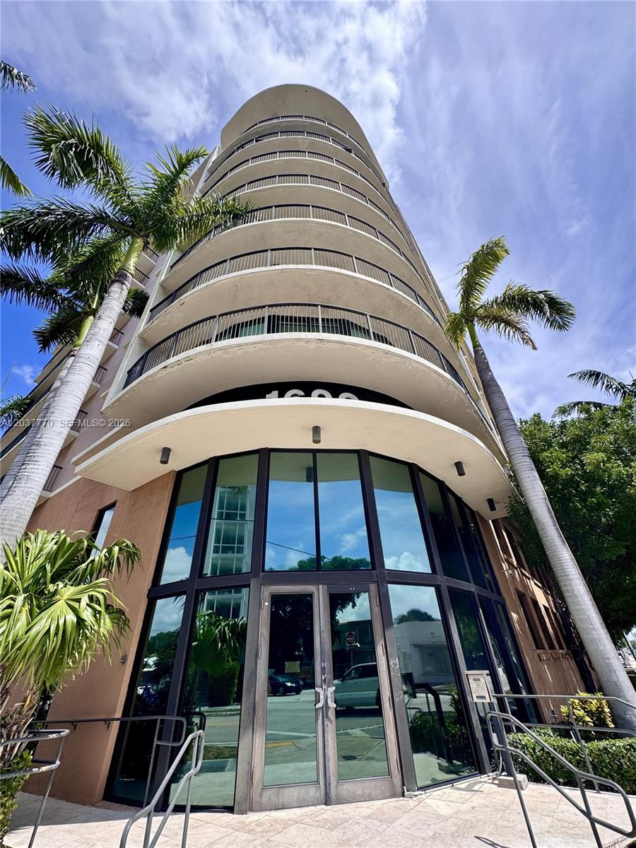 A low-angle view of a multi-story residential building with curved balconies and a glass entrance — 1690 SW 27th Ave # 502, Miami FL 33145, MIAMI, FL