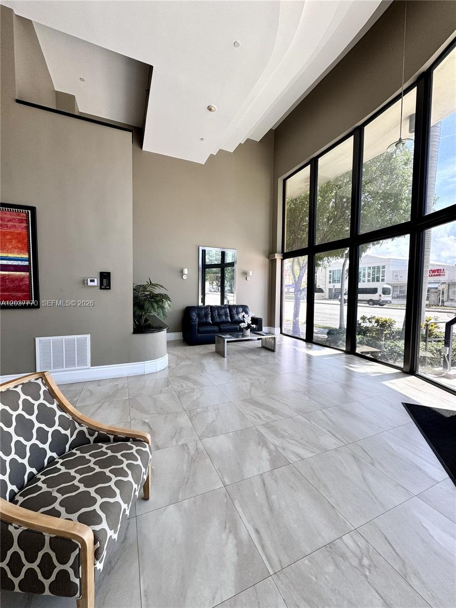 A modern lobby features tall windows, tiled floors, a black leather sofa, and patterned armchairs — 1690 SW 27th Ave # 502, Miami FL 33145, MIAMI, FL