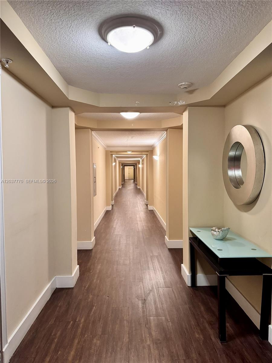 A long, narrow apartment hallway features wood-look flooring, beige walls, and recessed ceiling lights — 1690 SW 27th Ave # 502, Miami FL 33145, MIAMI, FL