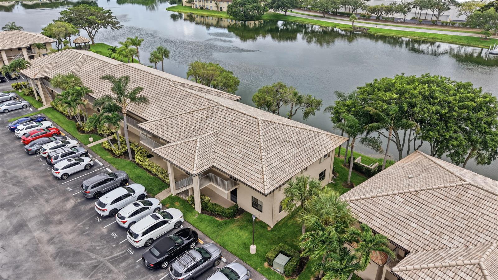 An aerial view shows a multi-story apartment building with a tiled roof beside a lake — 5501 Lakeside Drive # 207, Margate FL 33063, MARGATE, FL