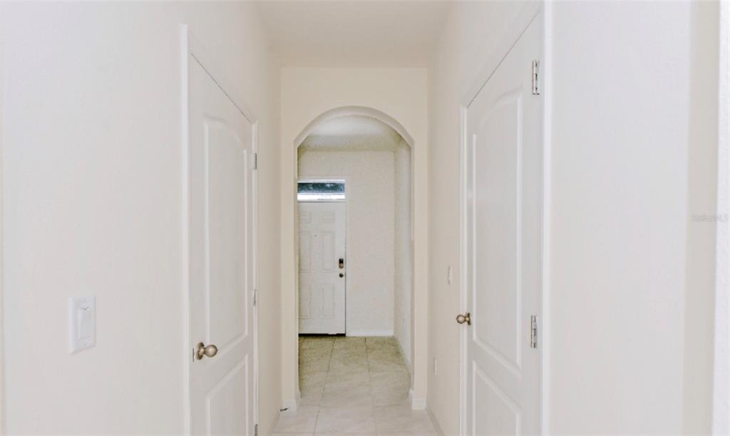 A hallway with white walls and doors leads to an arched entryway with tiled flooring — 1280 YELLOW FINCH DRIVE, DAVENPORT, FL