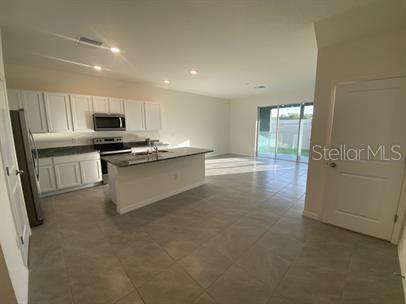 A kitchen with white cabinets and a center island opens into a spacious living area — 2906 SUNCOAST PLAINS DRIVE, ODESSA, FL