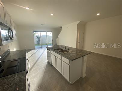 A kitchen with a granite-topped island, white cabinets, and tile flooring opens to a living area — 2906 SUNCOAST PLAINS DRIVE, ODESSA, FL