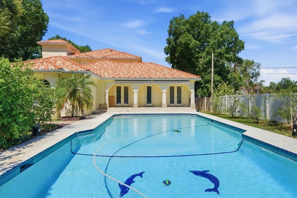 A swimming pool with dolphin mosaics sits in front of a house with a tiled roof — 12006 WATERSIDE COURT, TAMPA, FL
