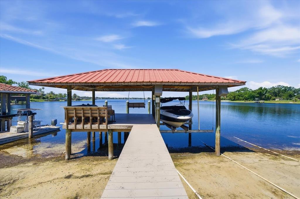 A covered boat dock with a boat lift sits on a sandy shoreline by water — 12006 WATERSIDE COURT, TAMPA, FL