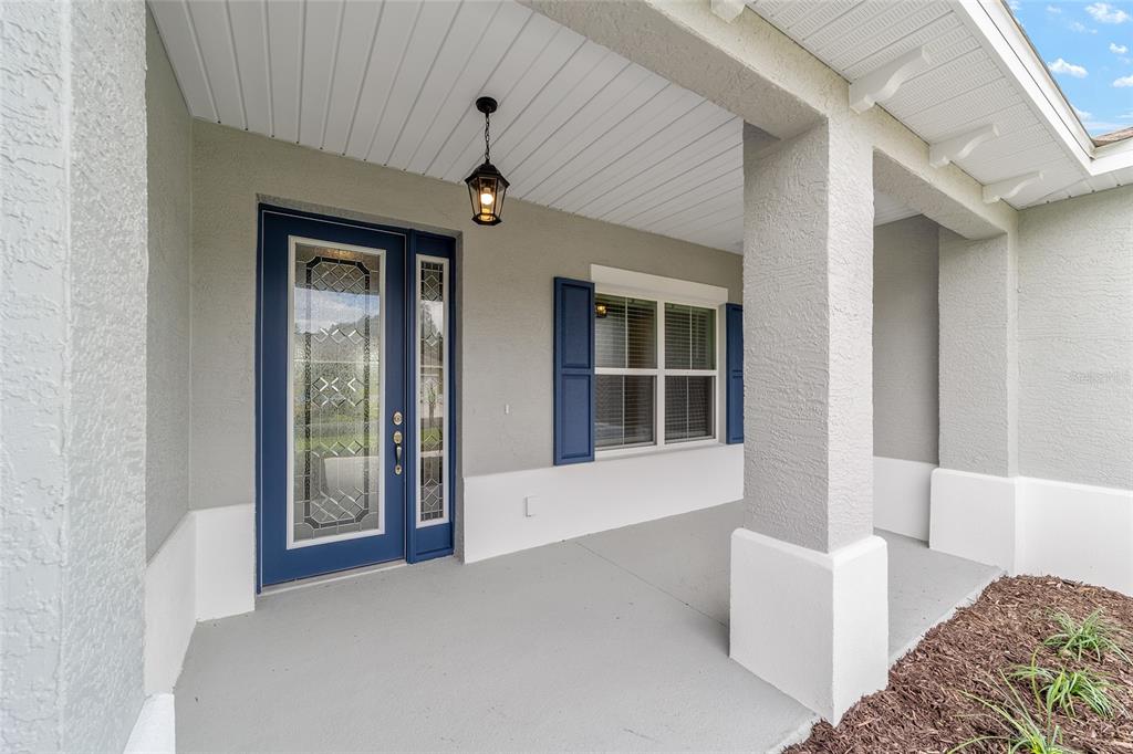 A covered front porch features a blue front door with glass panels and a window — 10358 SW 105TH COURT, OCALA, FL