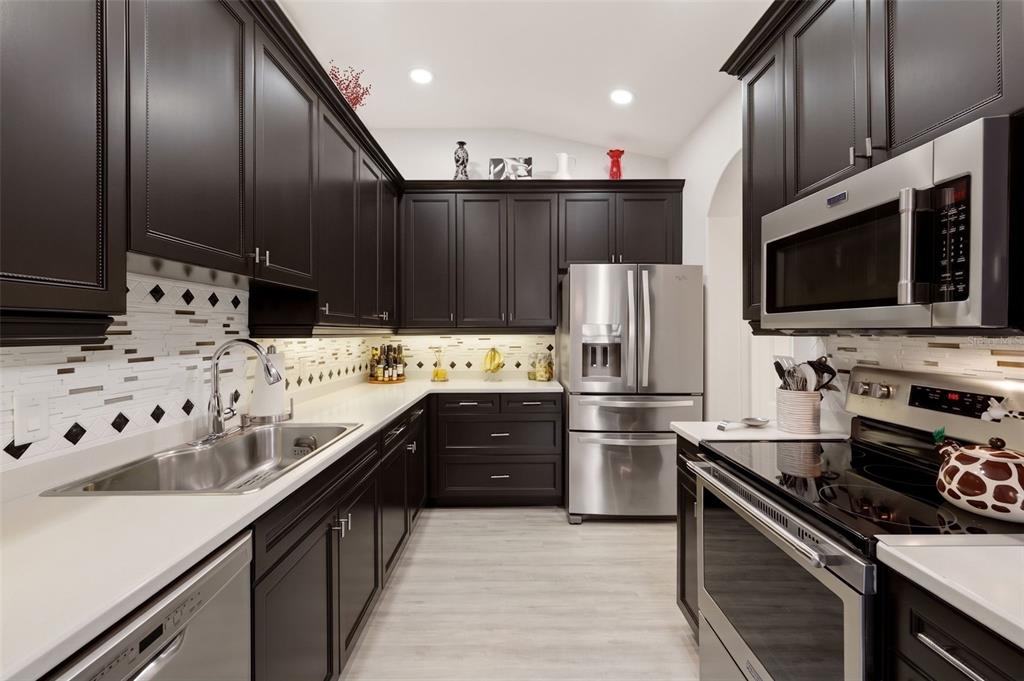 A kitchen features dark cabinetry, stainless steel appliances, white countertops, and a patterned tile backsplash — 1071 TOPELIS DRIVE, ENGLEWOOD, FL
