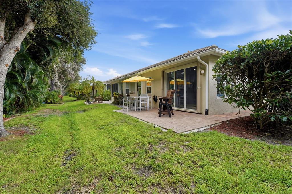 A paved patio with outdoor furniture sits behind a house next to a grassy yard — 1071 TOPELIS DRIVE, ENGLEWOOD, FL