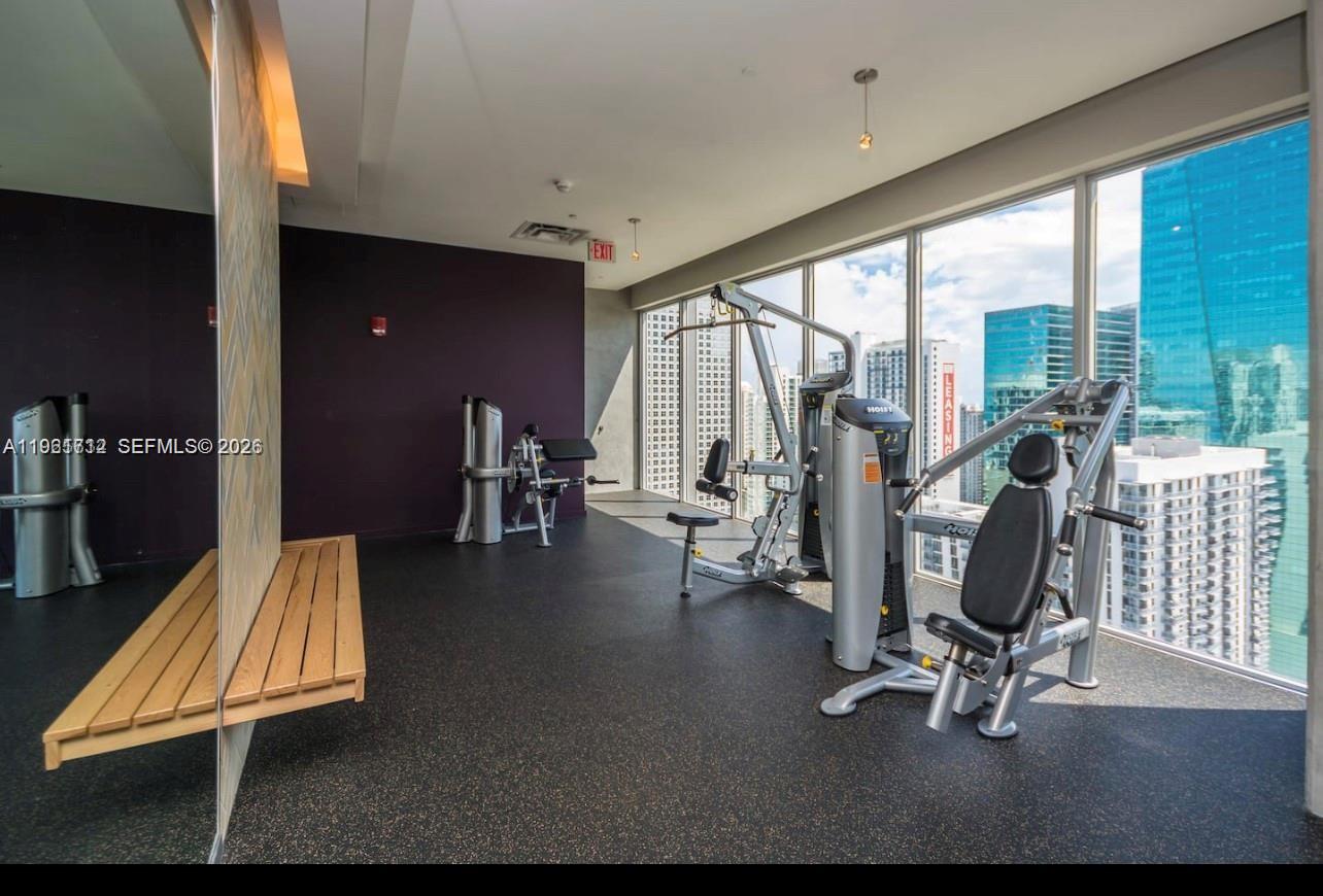 A gym with exercise machines, a wooden bench, and floor-to-ceiling windows overlooking a city skyline — 151 SE 1st St # 2104, Miami FL 33131, MIAMI, FL