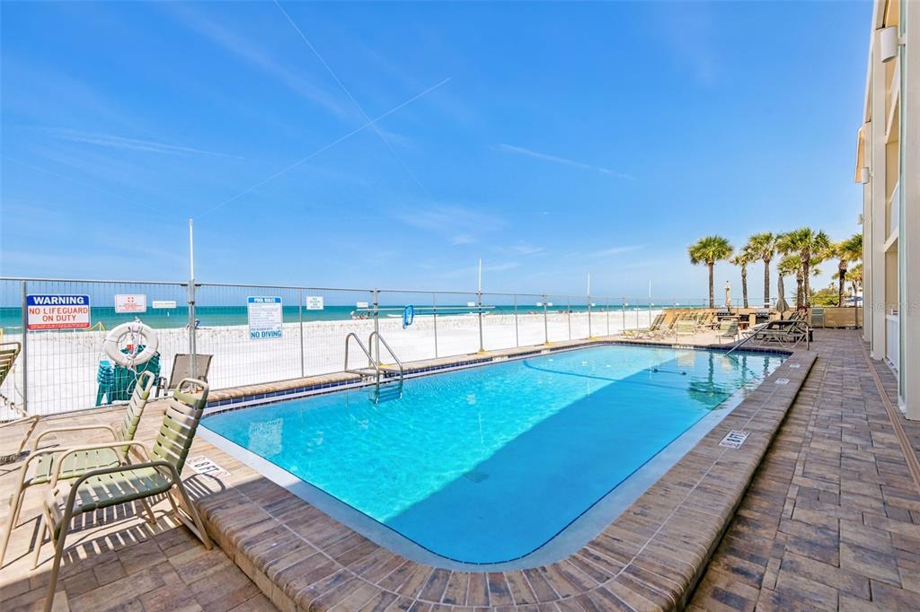 A rectangular swimming pool sits on a patio overlooking a sandy beach and ocean — 50 GULF BOULEVARD UNIT 301, INDIAN ROCKS BEACH, FL