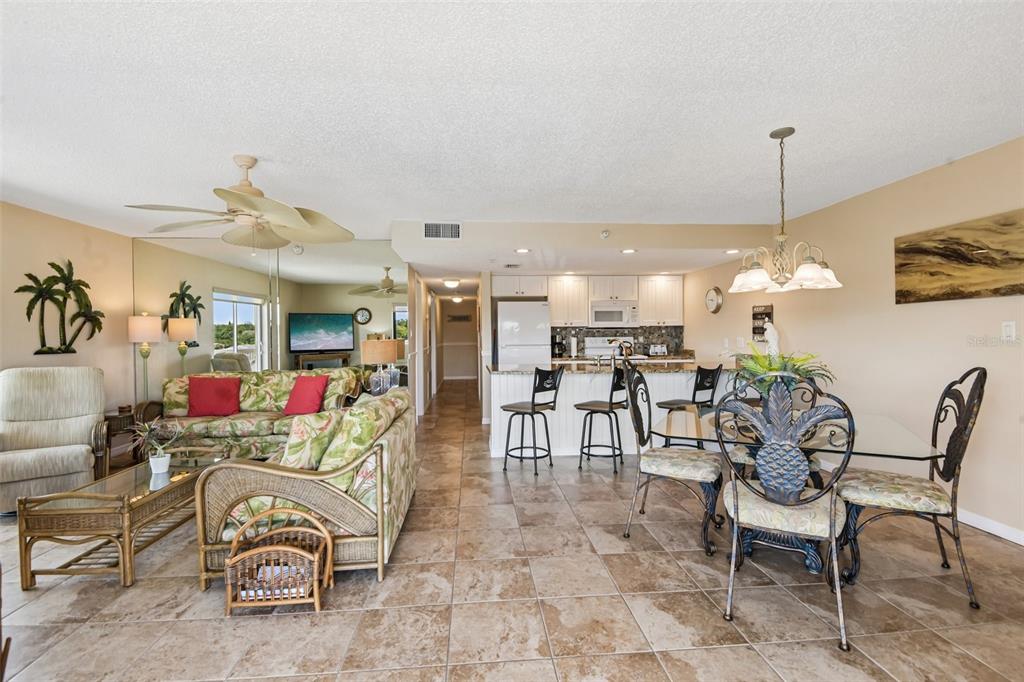 An open-concept living and dining area features tile flooring, a kitchen island, and tropical decor — 50 GULF BOULEVARD UNIT 301, INDIAN ROCKS BEACH, FL