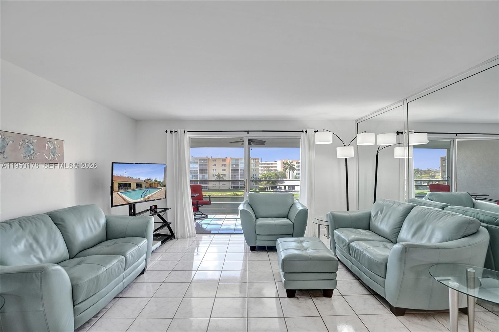 A living room features light blue leather furniture, white tile floors, and a mirrored wall — 200 SE 5th Ave # 405, Dania Beach FL 33004, DANIA BEACH, FL