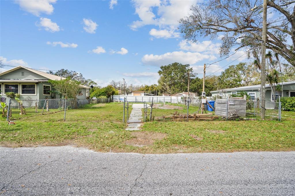 A vacant, fenced-in residential lot sits between two single-story houses under a blue sky — 12912 CAMBRIDGE AVENUE, TAMPA, FL