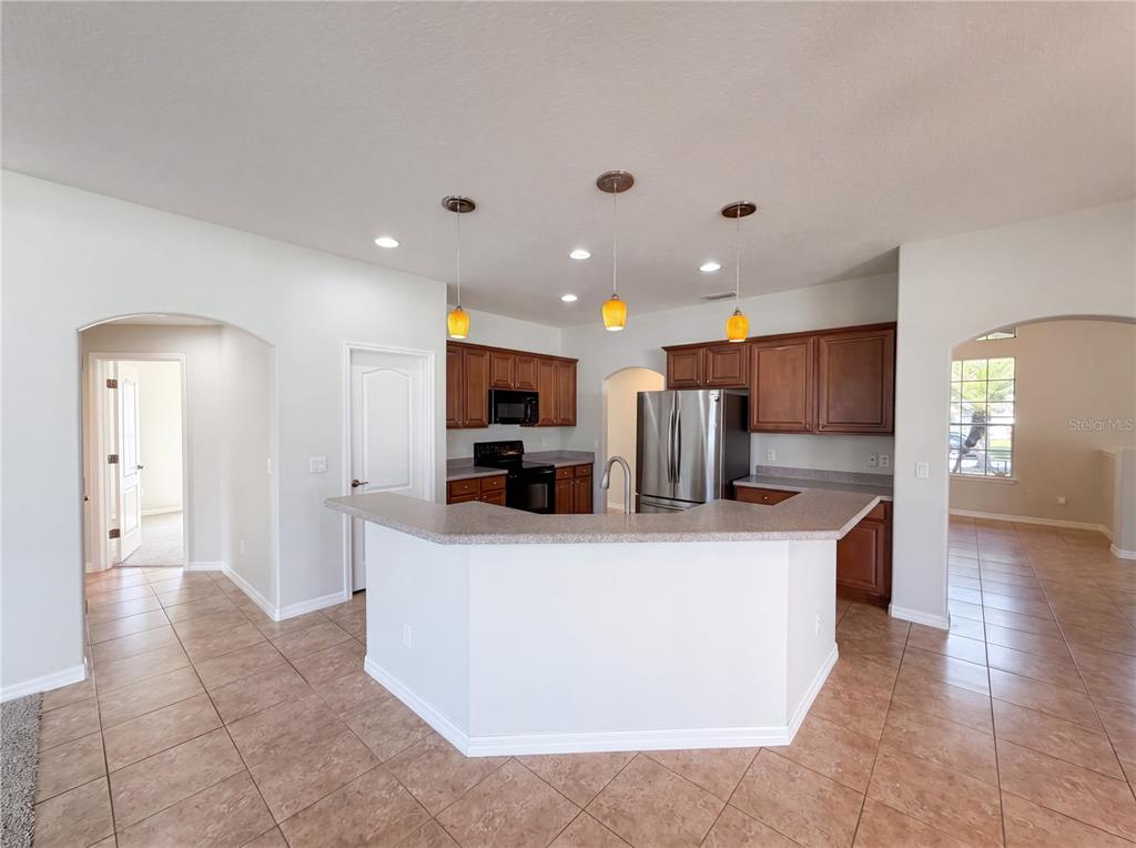 A kitchen features a peninsula, stainless steel appliances, brown cabinets, and light-colored tile flooring — 457 AMETHYST AVENUE, AUBURNDALE, FL