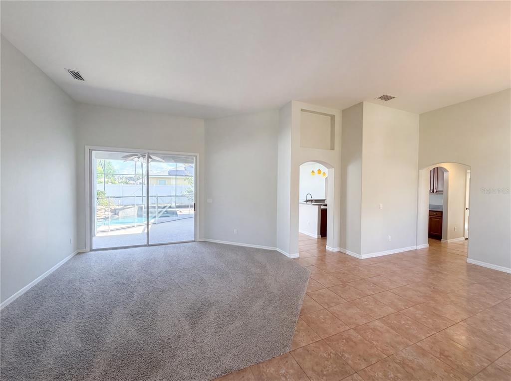 A living room with carpeted flooring, sliding glass doors to a pool, and tiled walkways — 457 AMETHYST AVENUE, AUBURNDALE, FL