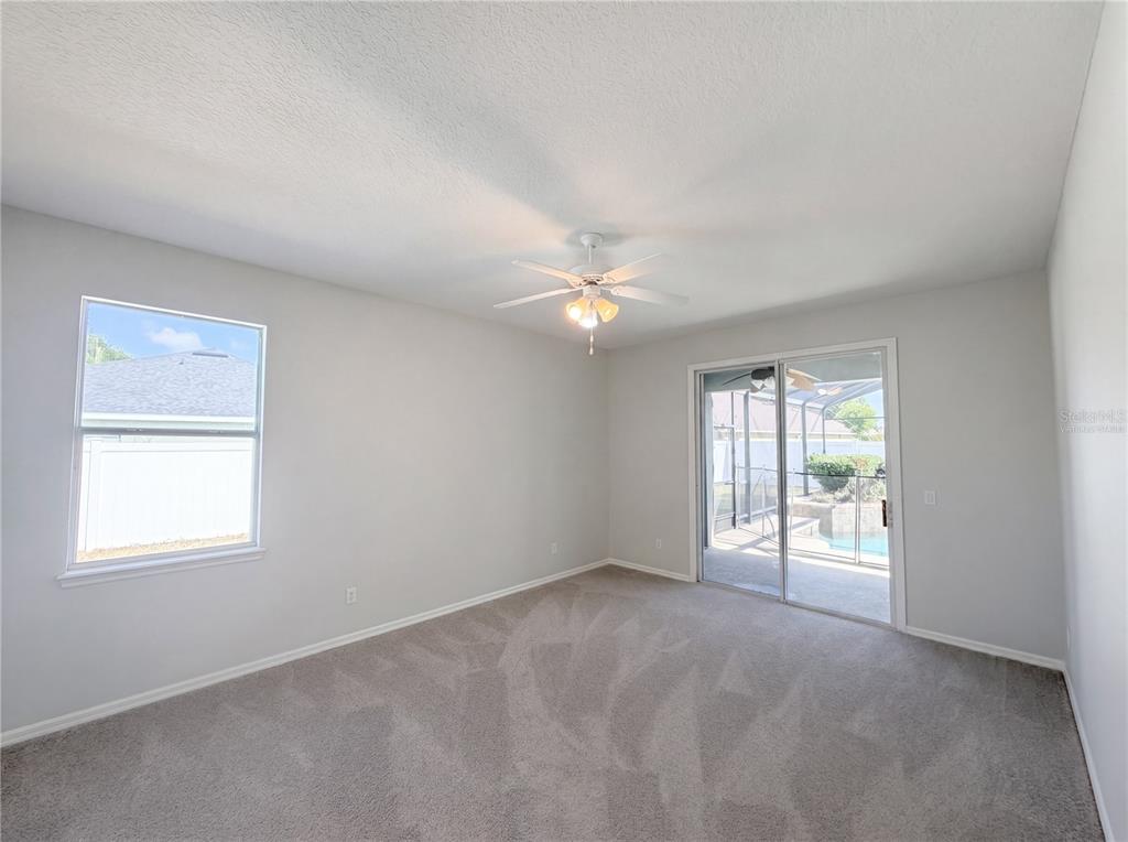 A carpeted bedroom with a ceiling fan, a single window, and sliding glass patio doors — 457 AMETHYST AVENUE, AUBURNDALE, FL